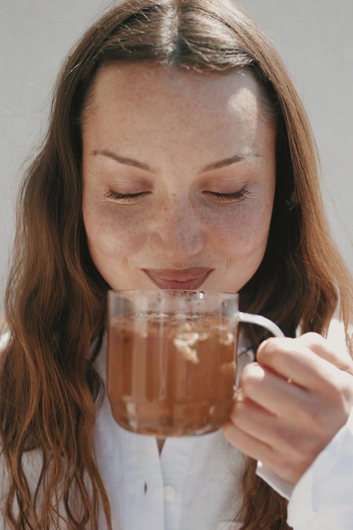 Une femme, les yeux fermés, respire le parfum de sa tasse d'infusion