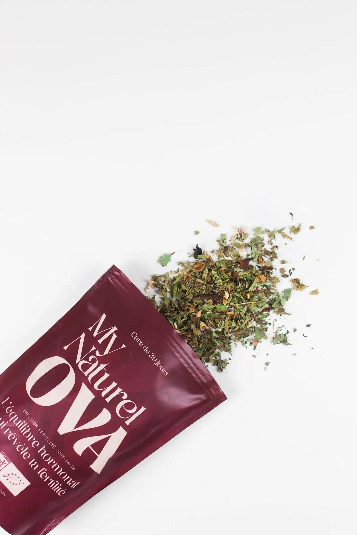 Le sachet My Naturel Ova ouvert, les plantes séchées se répandent sur un fond blanc
