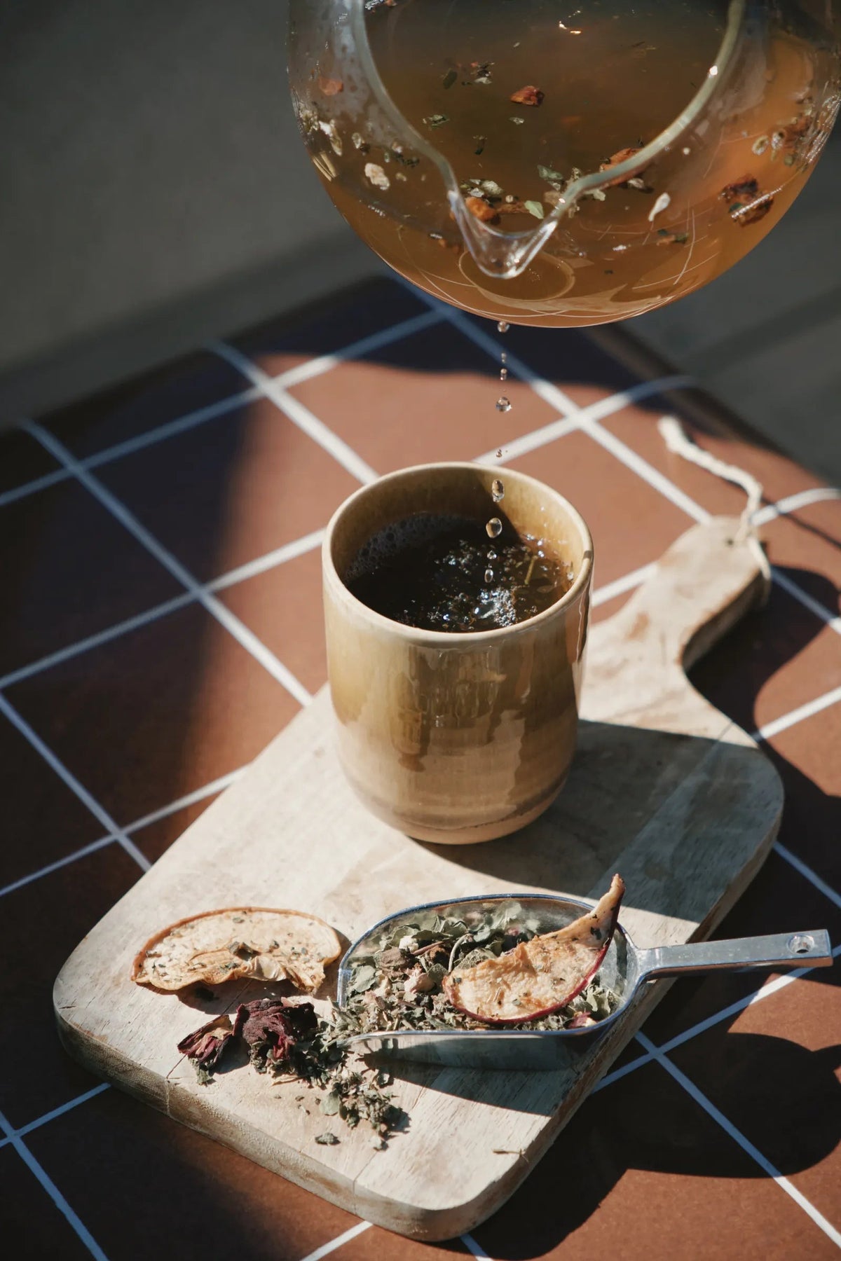 Une théière verse l'infusion dans une tasse, à côté d'une cuillère de plantes